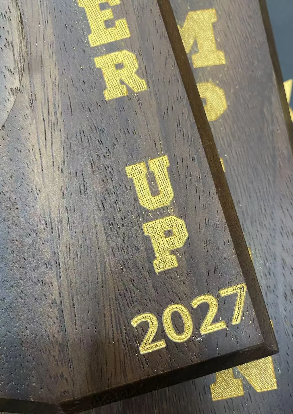 Macro view of gold-fill lettering on a dark wood trophy component